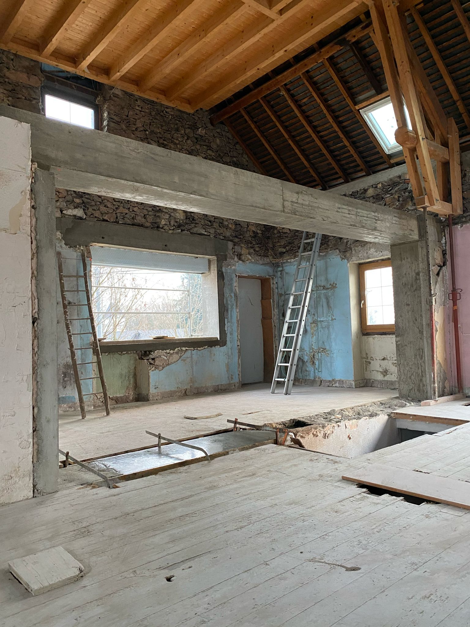 Intérieur d'une grange en rénovation lourde : poutres béton, charpente et reprise de plancher